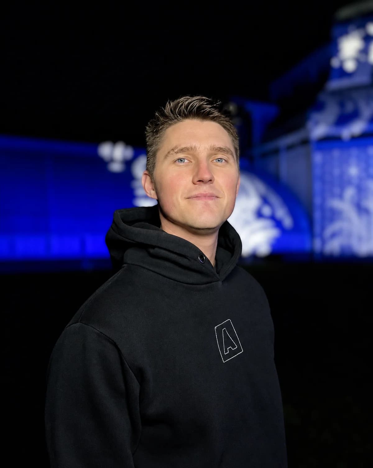 Oleksandr in a black hoodie against a blue-lit venue background